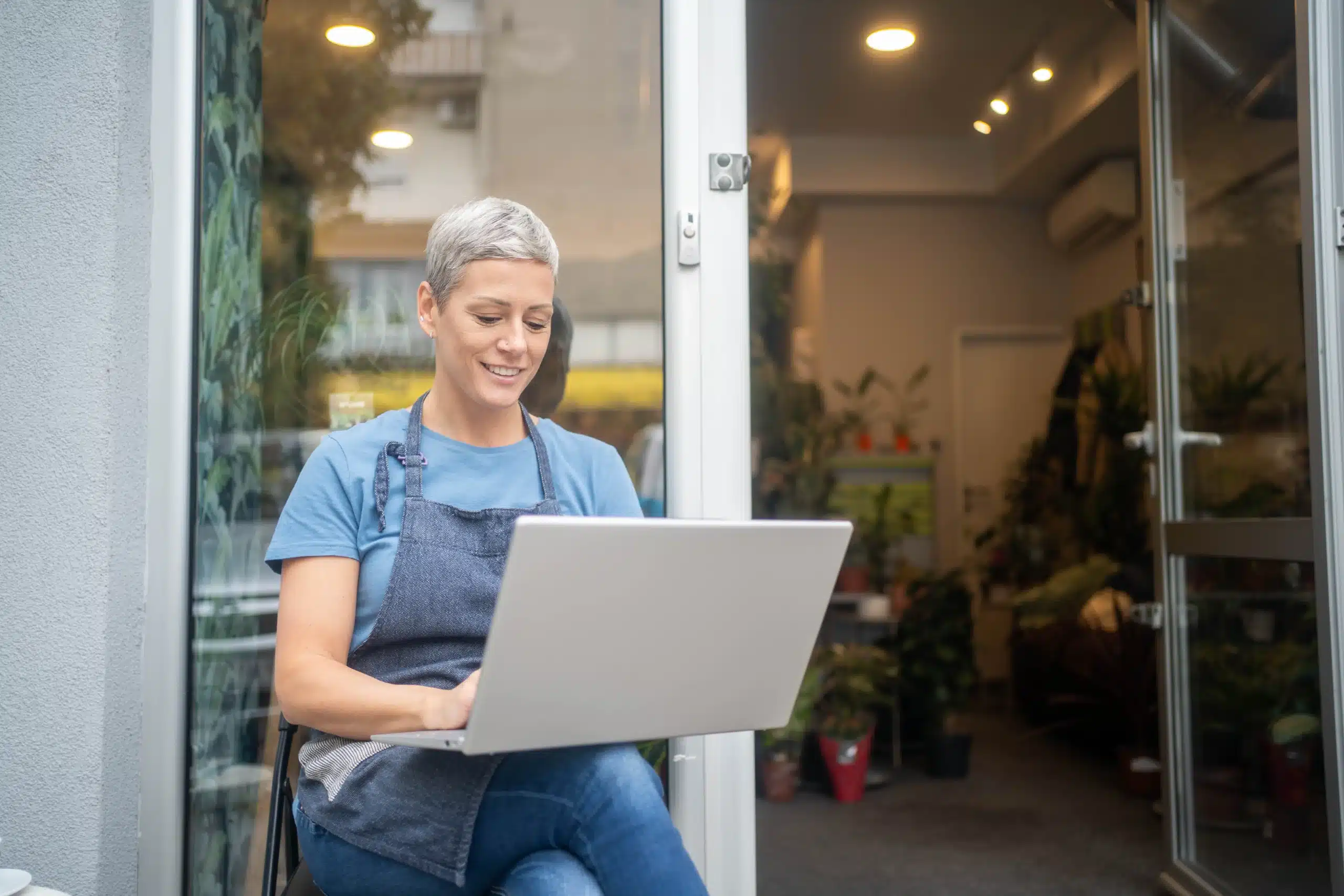 seo-guide-small-business-owner-laptop A cheerful small business owner sitting outside her flower shop reviewing her online orders on a laptop, illustrating how small businesses can grow with SEO
