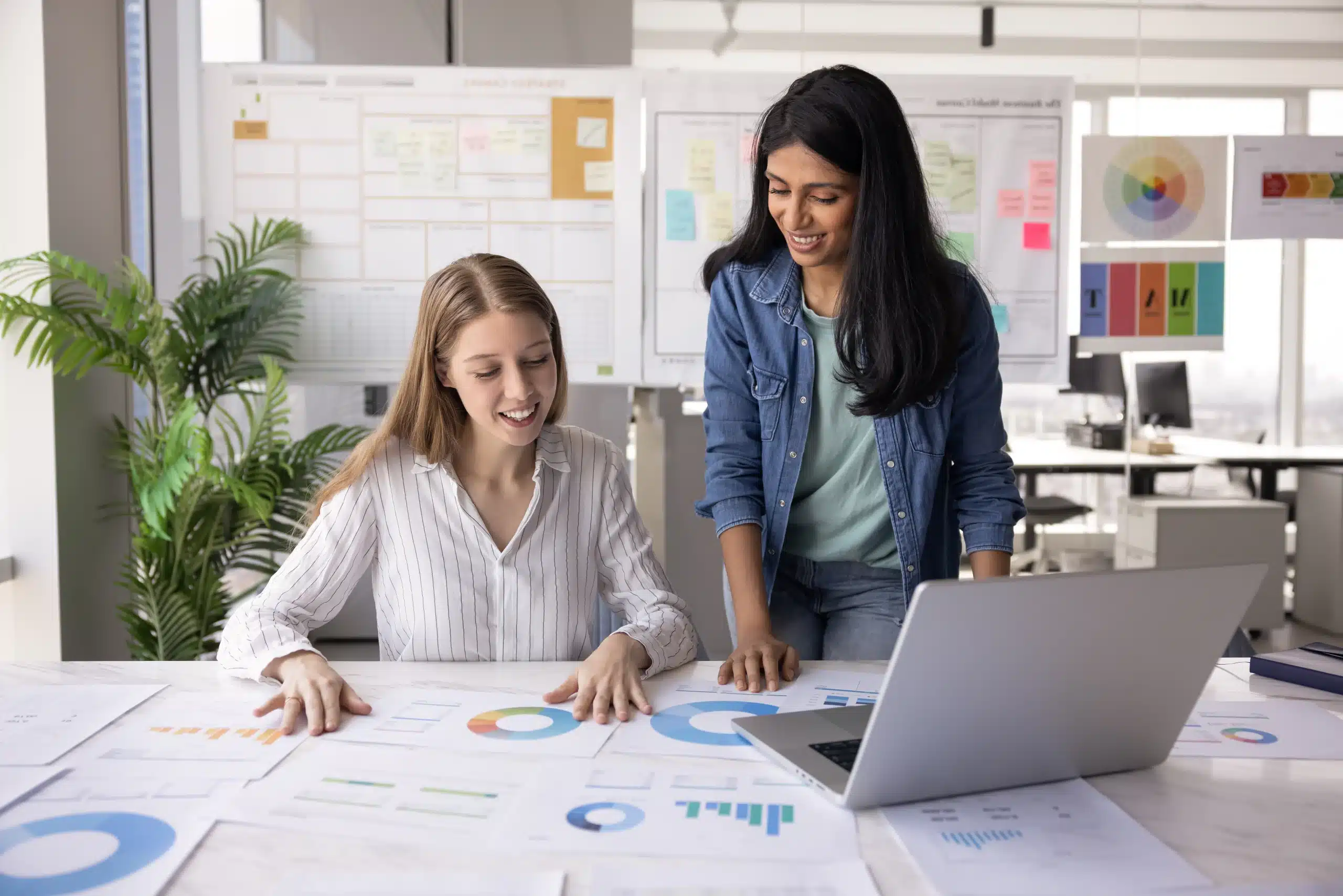 Two professional women working on visual data at conference table Marketing professional reviewing bilingual ad content for a Hispanic audience campaign