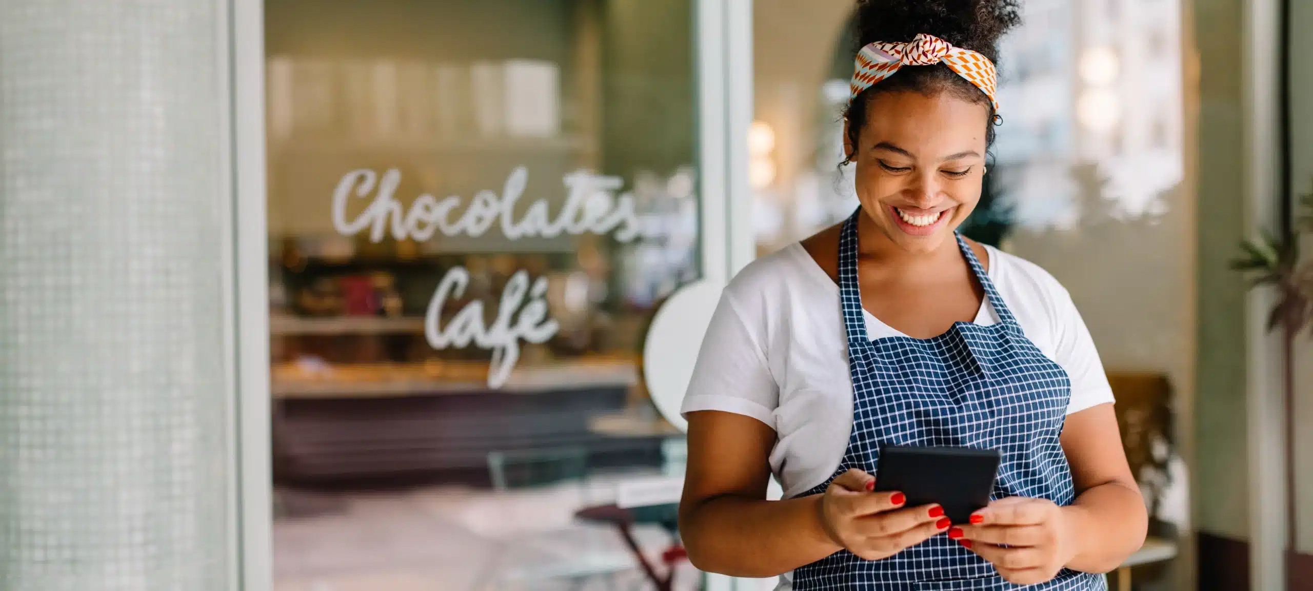 Happy female entrepreneur smiling with digital tablet and smartphone in her cafe Empresaria latina sonriendo con tableta y teléfono en su negocio.